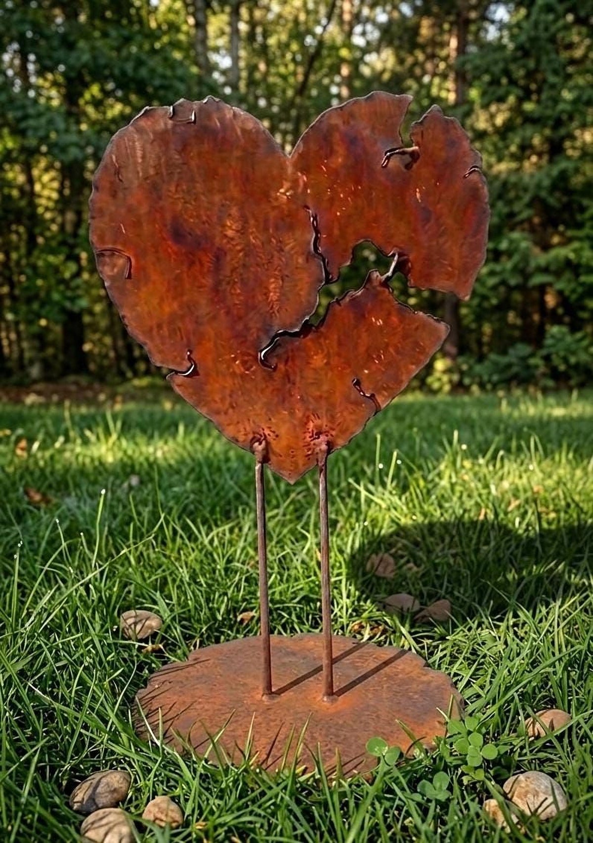 A rusted metal heart sculpture stands in a grassy area, surrounded by small rocks.