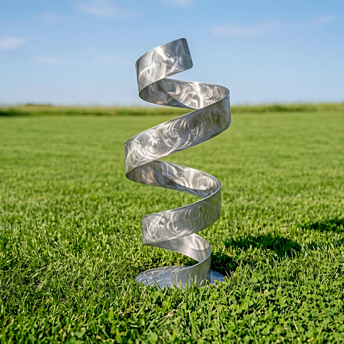 A silver spiral sculpture stands in a grassy field, its intricate design and metallic sheen contrasting with the natural surroundings.