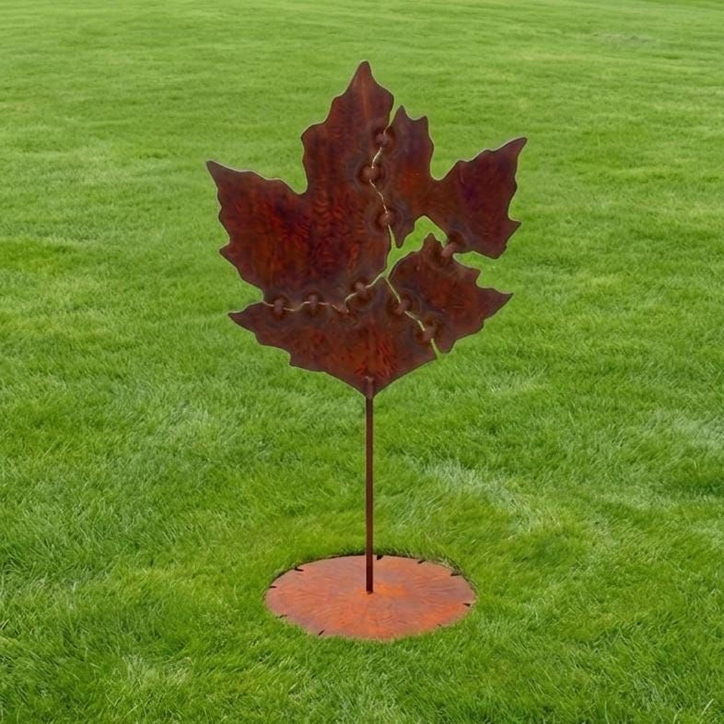 A large, rusted metal sculpture of a leaf stands in a grassy field.