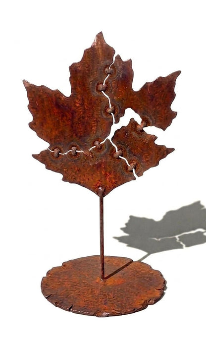 a rust-colored metal sculpture of a leaf, with a circular base and a vertical stem.