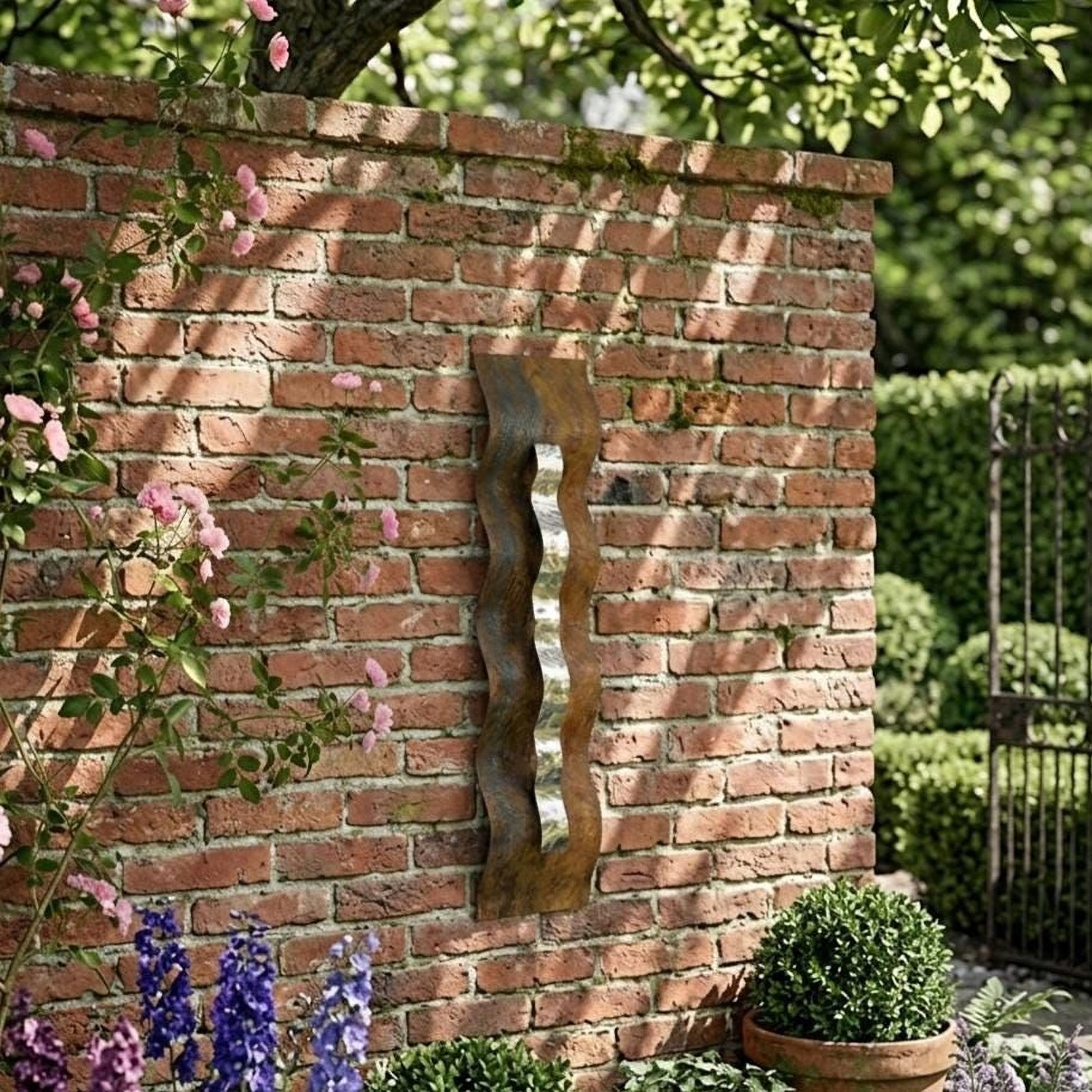 A rustic brick wall with a wavy metal sculpture attached to it, surrounded by lush greenery and vibrant flowers.