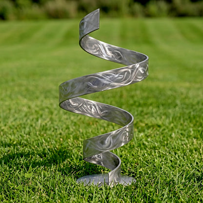 A metal spiral sculpture stands on a grassy lawn, its intricate design and curved form creating a visually striking contrast against the natural backdrop.