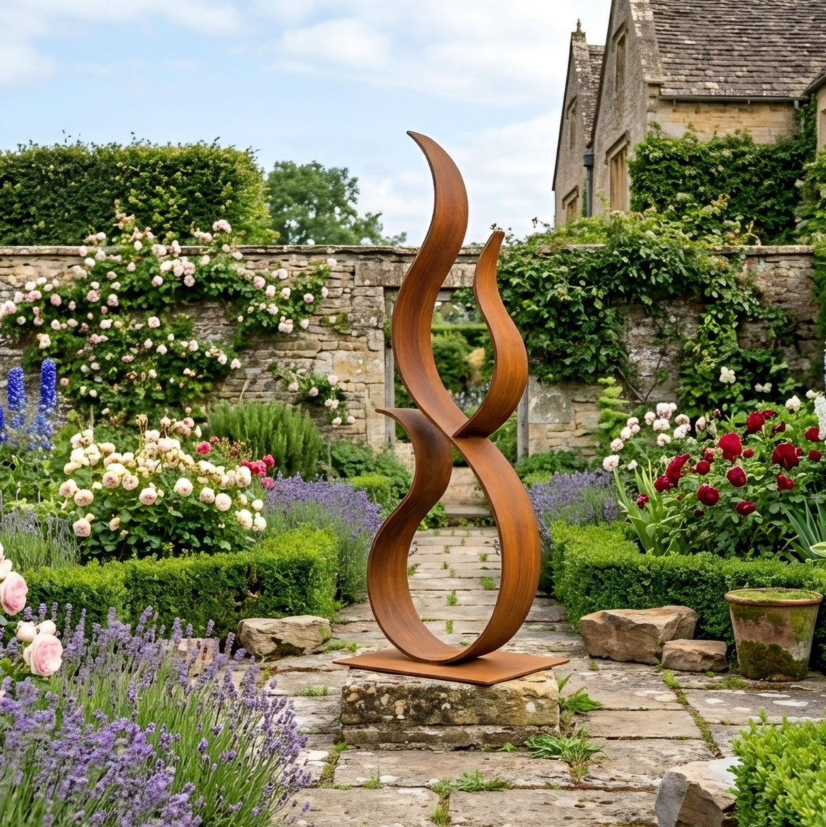 A large, abstract metal sculpture resembling a flame or fire stands in a lush, colorful garden surrounded by various flowers and plants.