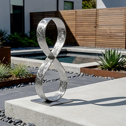 a modern outdoor sculpture composed of a metallic ring-like structure, placed on a concrete pedestal in a garden setting.