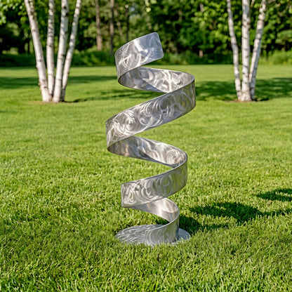 A silver spiral sculpture stands on a grassy lawn, surrounded by trees.