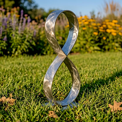 A metallic sculpture resembling an infinity symbol stands in a grassy area with colorful flowers in the background.