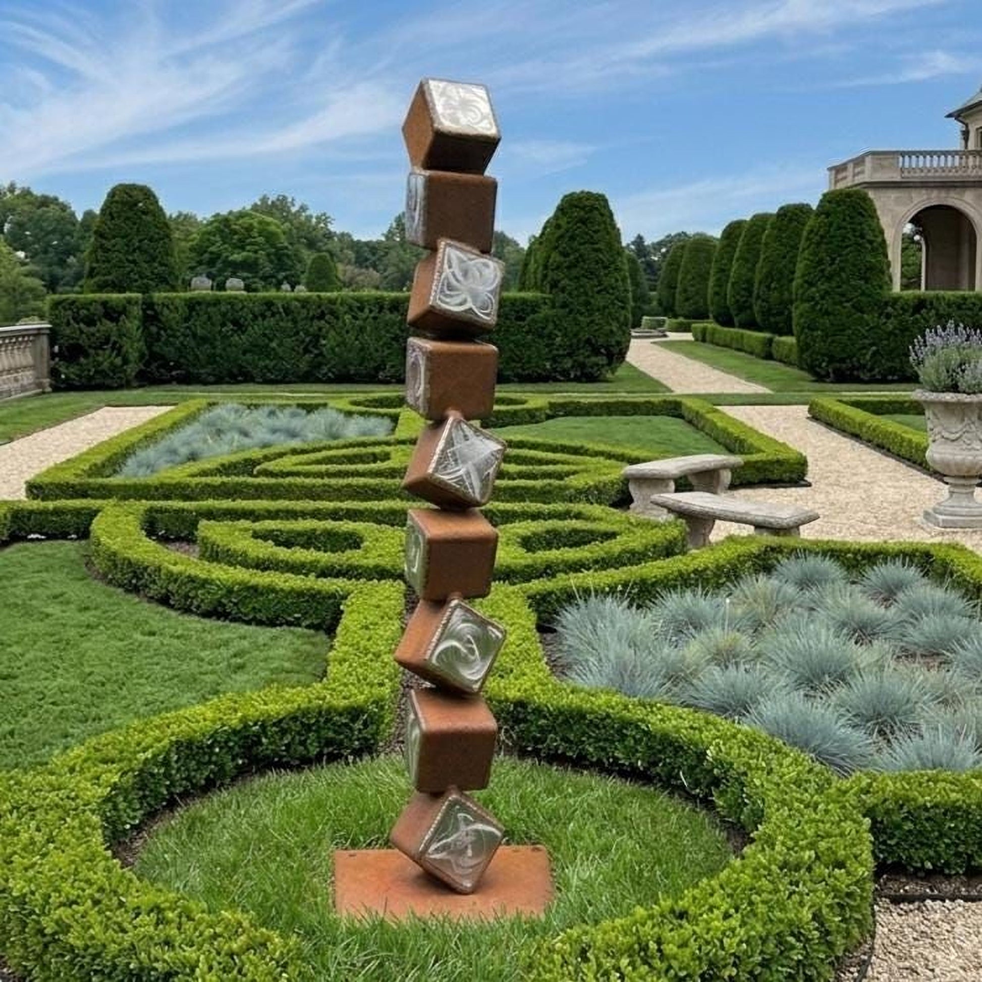 A tall, abstract sculpture made of stacked cubes stands in a meticulously maintained garden, surrounded by neatly trimmed hedges and a variety of plants.