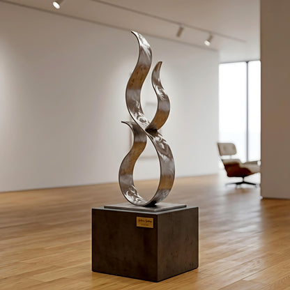a modern art sculpture of a metallic flame-like shape, displayed on a black pedestal in an art gallery setting.