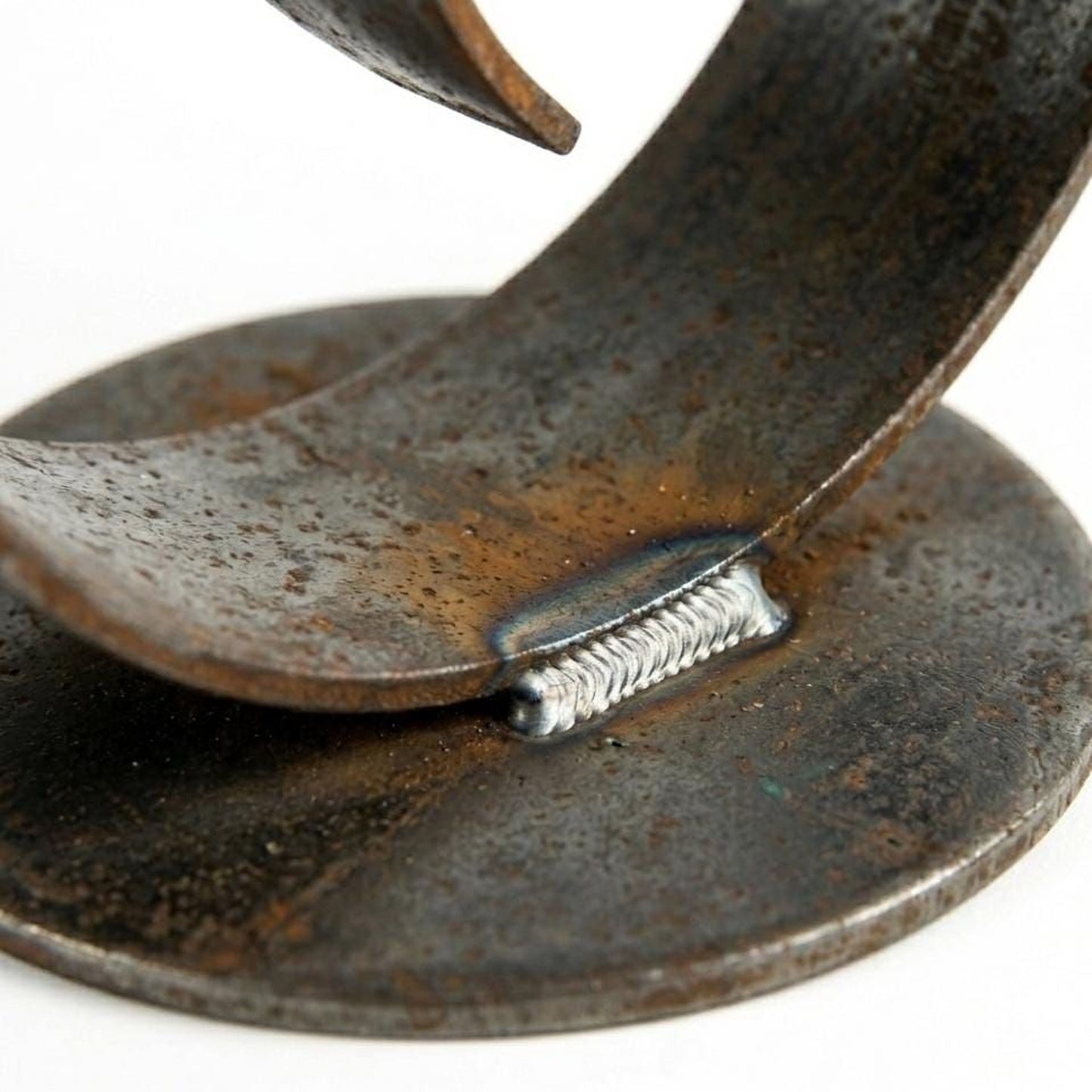 A close-up view of a rusted metal surface with a metal joint, likely a welded connection, and a circular metal plate or base.