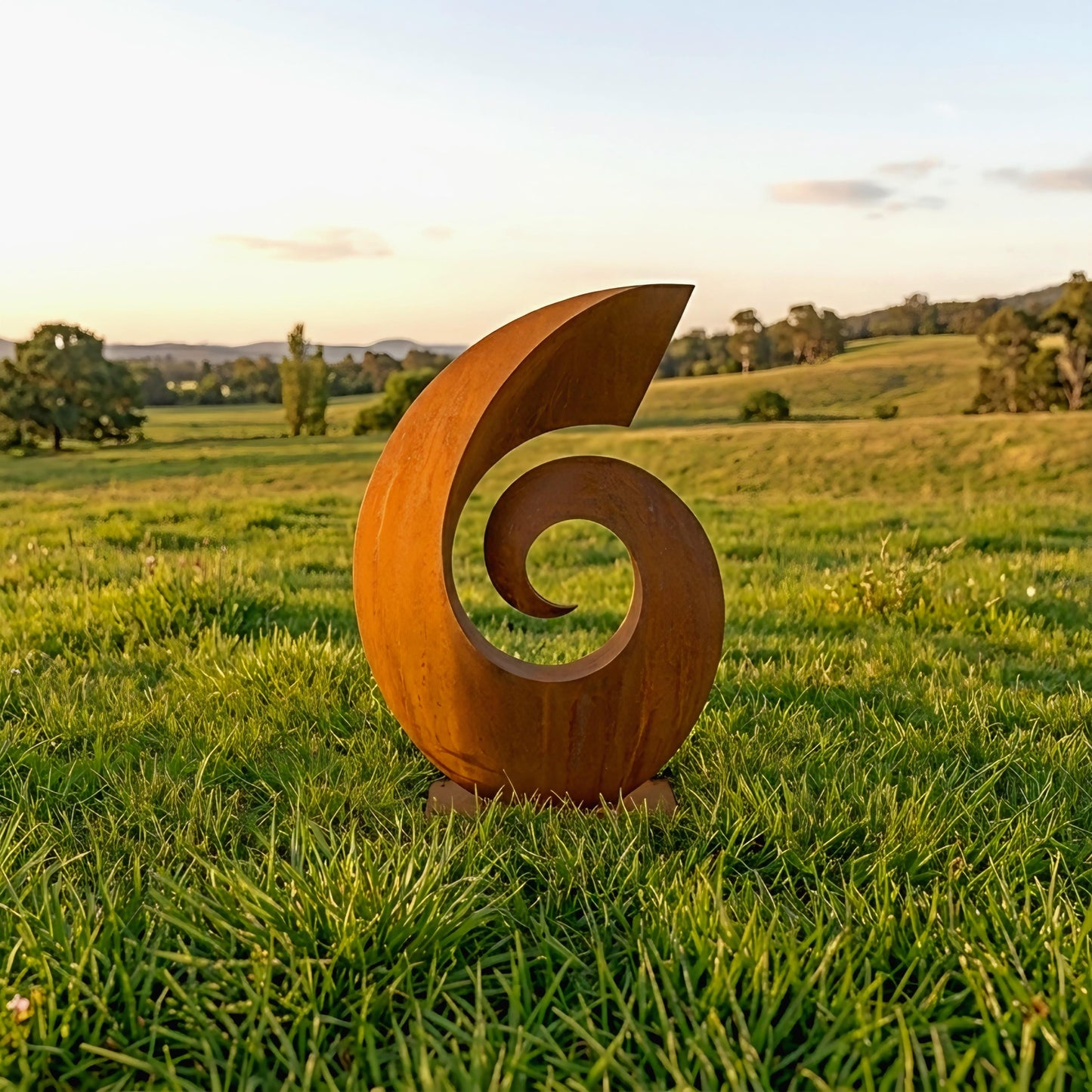a large, abstract sculpture made of a curved, orange material, standing in a grassy field with trees and hills in the background.