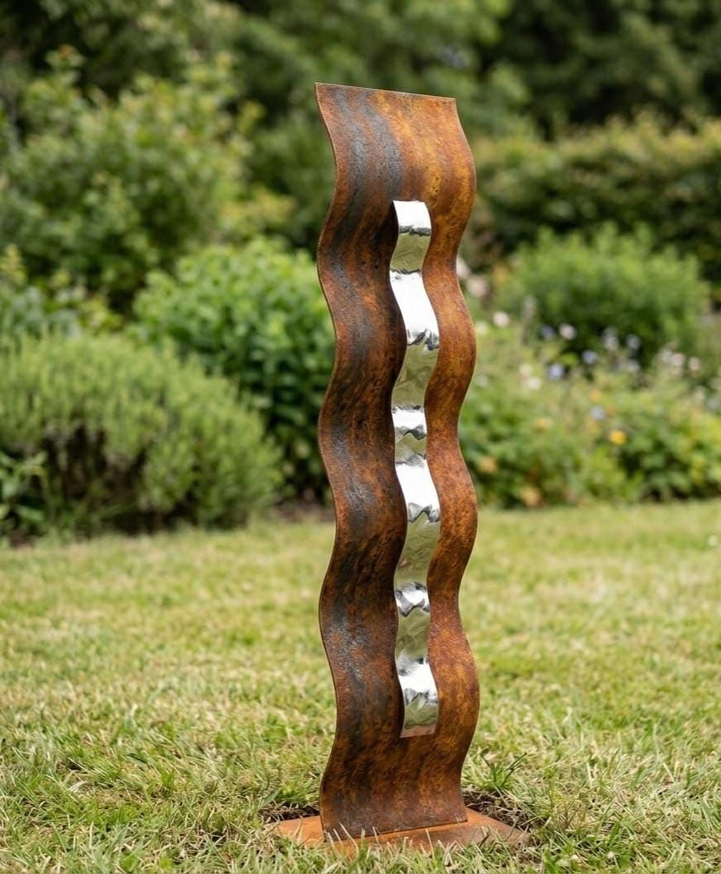 A tall, rust-colored metal sculpture with a curved, wavy design stands in a grassy area surrounded by greenery.