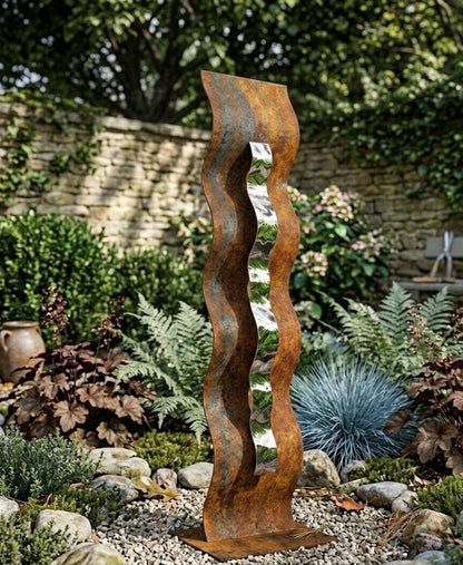 a tall, rust-colored metal sculpture with a vertical, wavy design, standing in a garden surrounded by various plants and rocks.