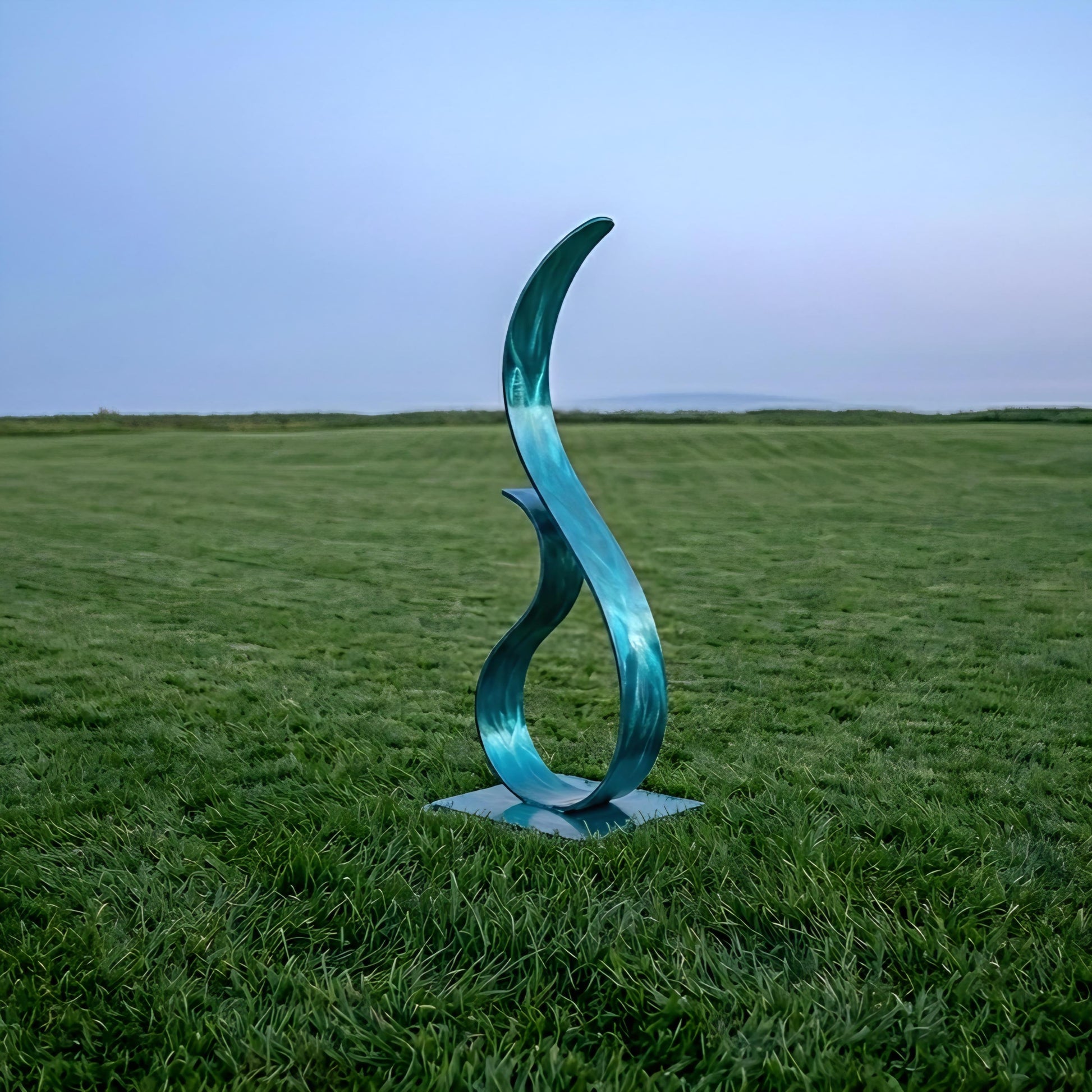A blue metal sculpture resembling a flame stands in a grassy field, with a clear blue sky in the background.