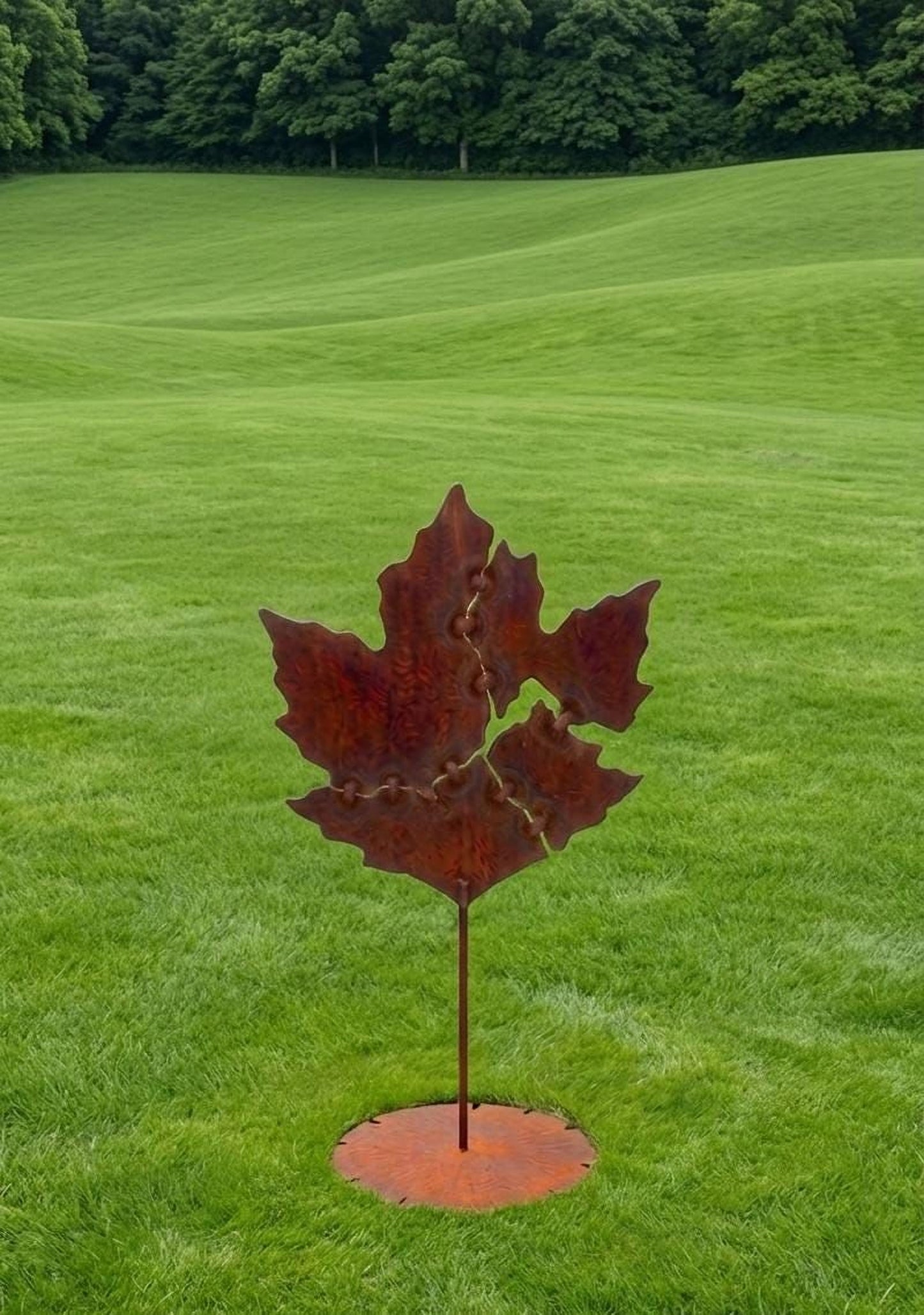 A large, rusted metal sculpture of a leaf stands in a grassy field, surrounded by trees.