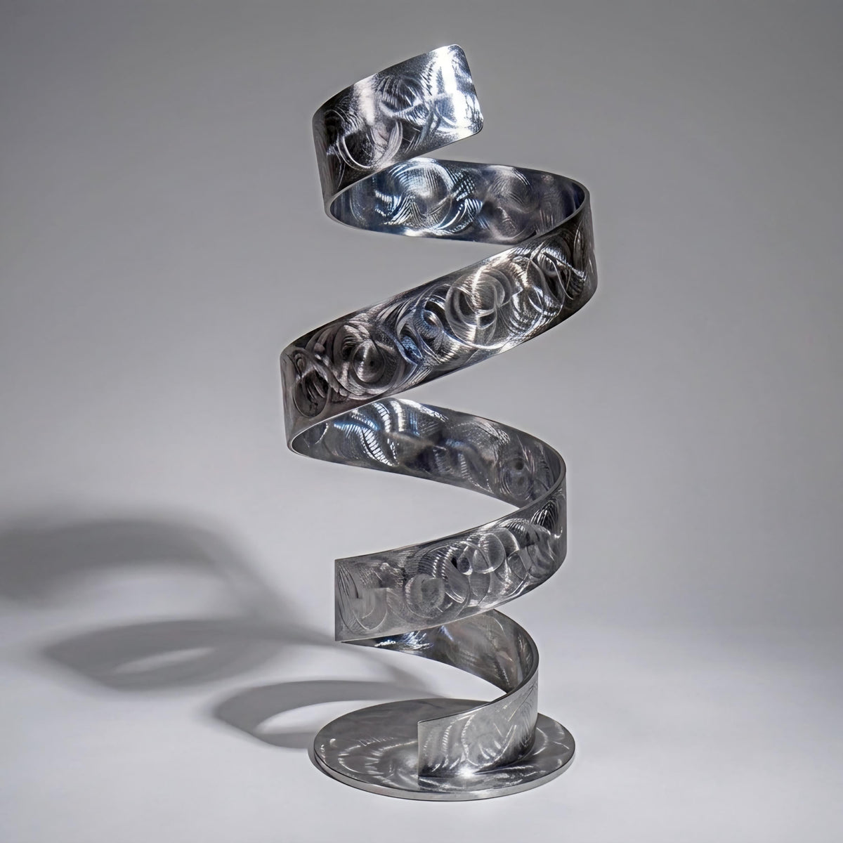 A spiral metal sculpture with a repeating pattern of circles and lines, standing on a round base.