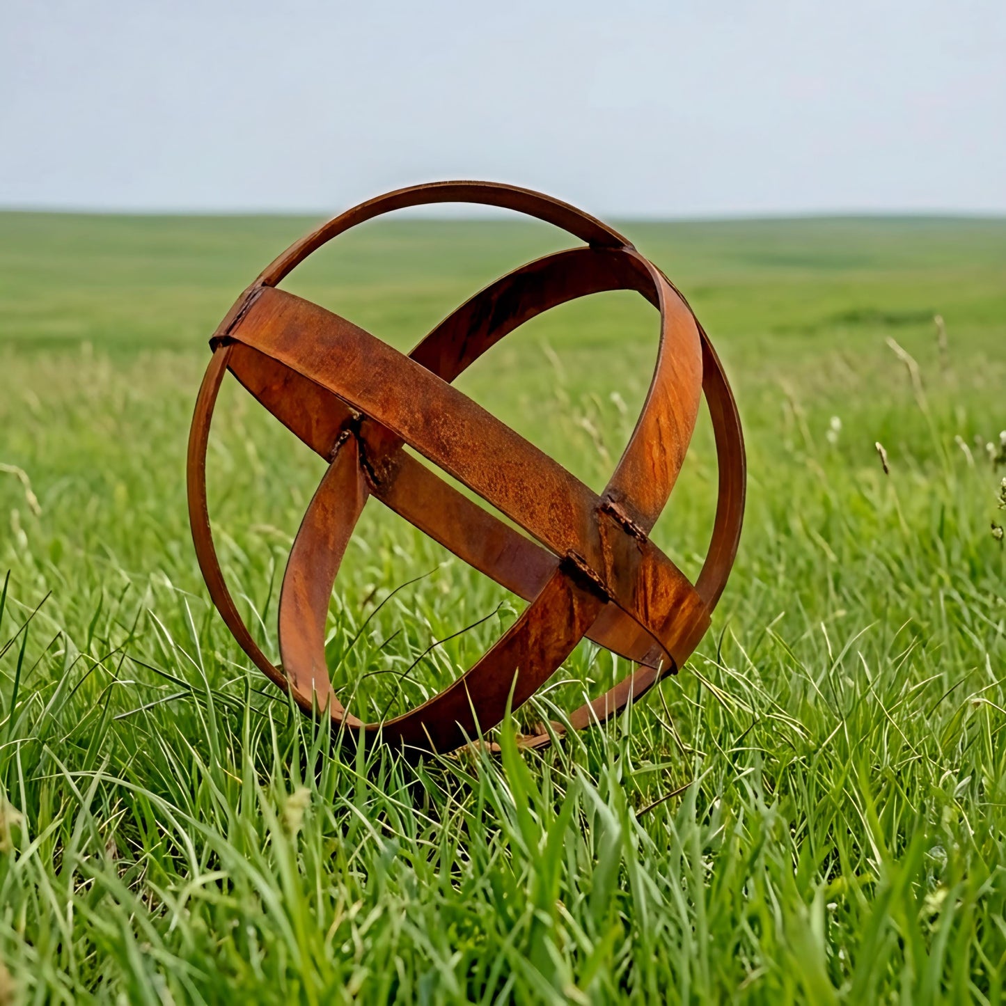 An orange metal sculpture resembling a sphere or ball rests in a grassy field.