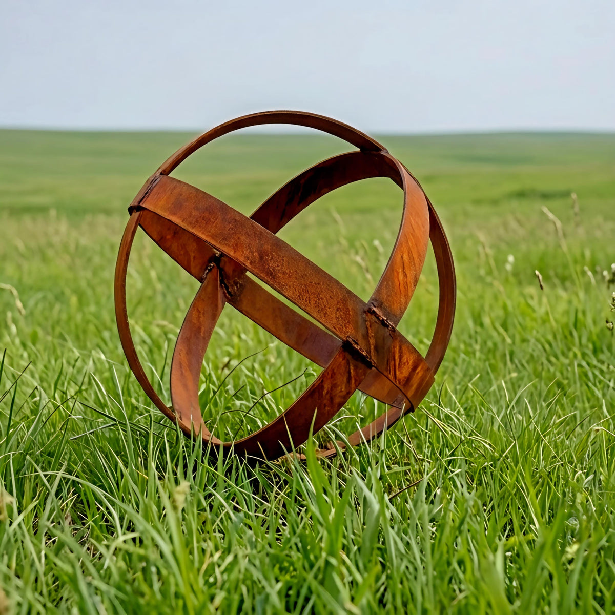 An orange metal sculpture resembling a sphere or ball rests in a grassy field.