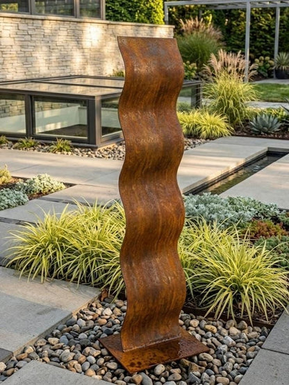 a tall, rust-colored metal sculpture with a wavy, textured design, situated in a garden setting with various plants and rocks.
