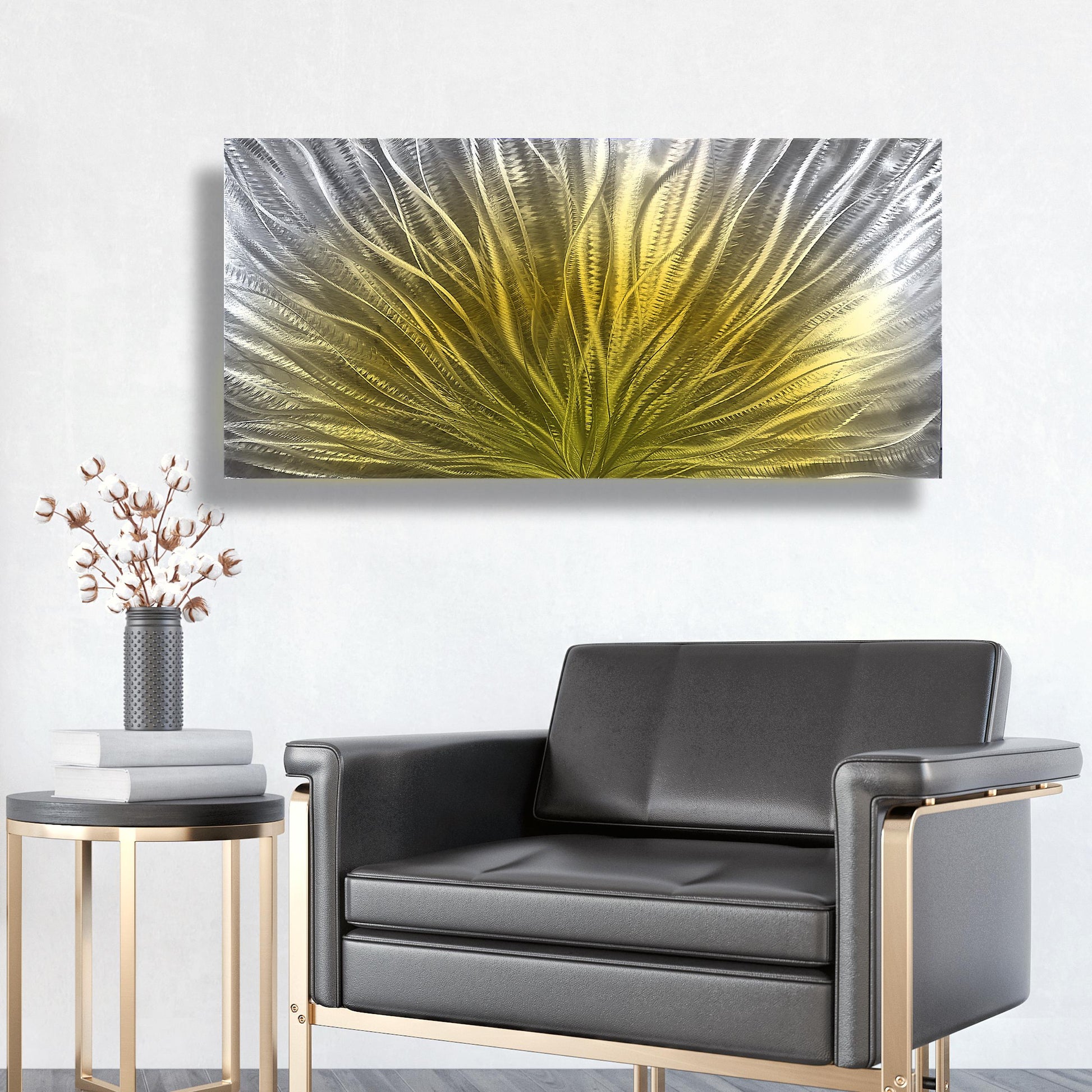 May include: A large, rectangular metal wall art piece with an abstract design. The artwork features a central burst of yellow, transitioning to silver and grey on the edges. It's mounted on a white wall above a black leather armchair.