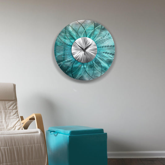 May include: A circular teal metal wall clock with a silver centre and black hands. The clock features a textured, floral design. The clock is mounted on a white wall.