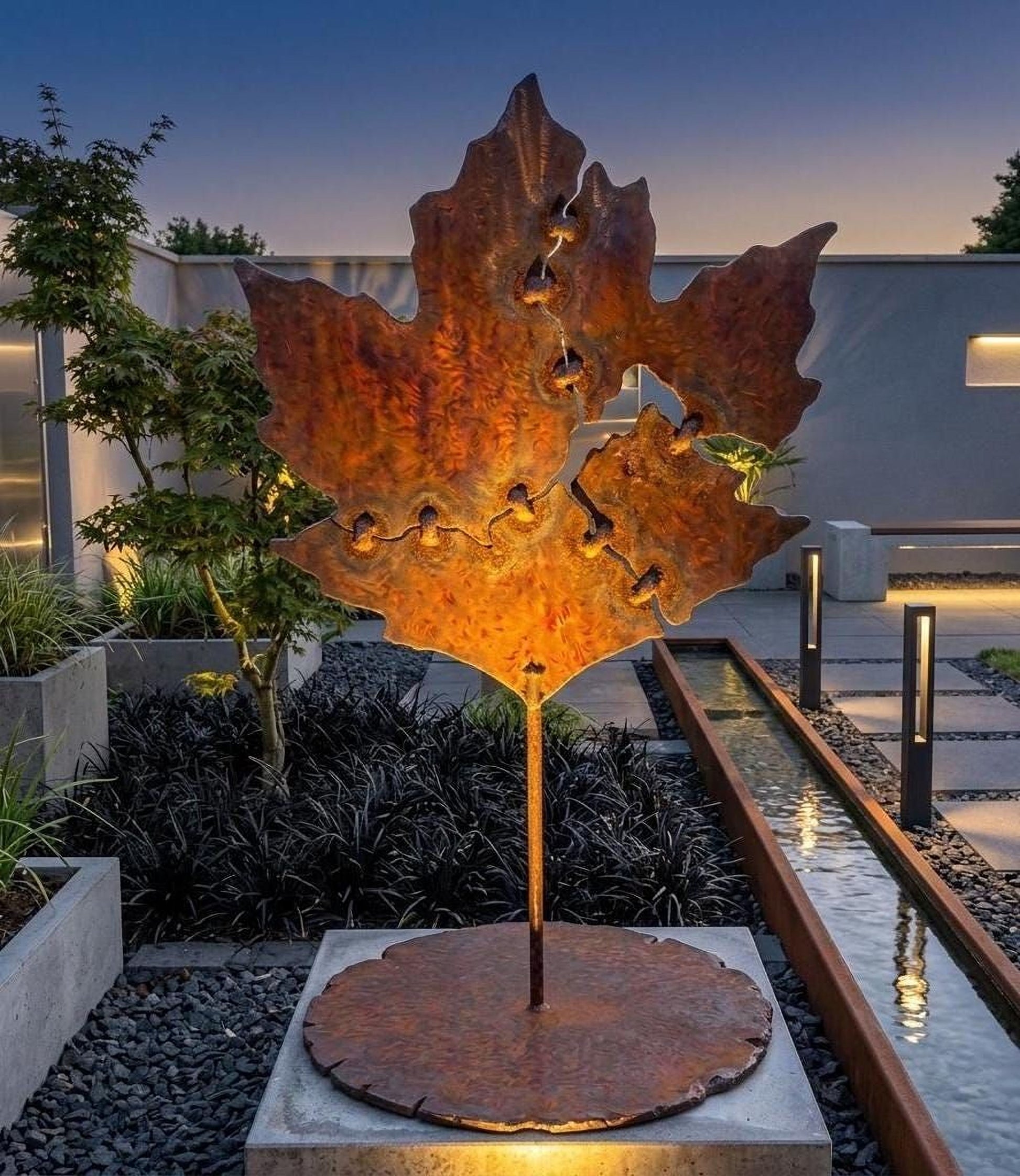 a large, rust-colored metal sculpture of a leaf, illuminated by a warm light, situated in a garden setting with a pond and plants in the background.