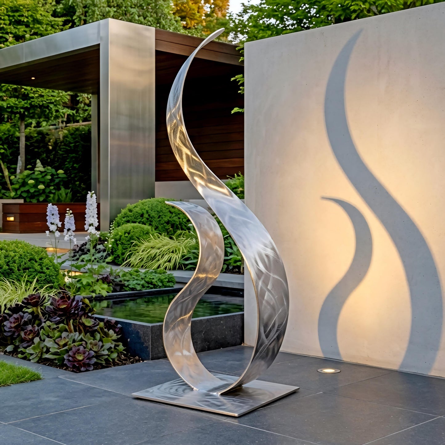 a modern, metallic sculpture with a unique, curved design, situated in a garden setting with a pond and lush greenery in the background.