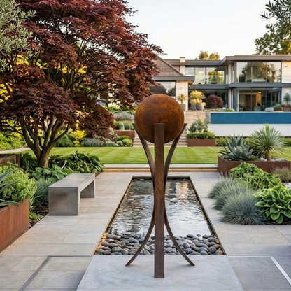 A modern garden with a large metal sculpture in the center, surrounded by lush greenery and a tranquil water feature.