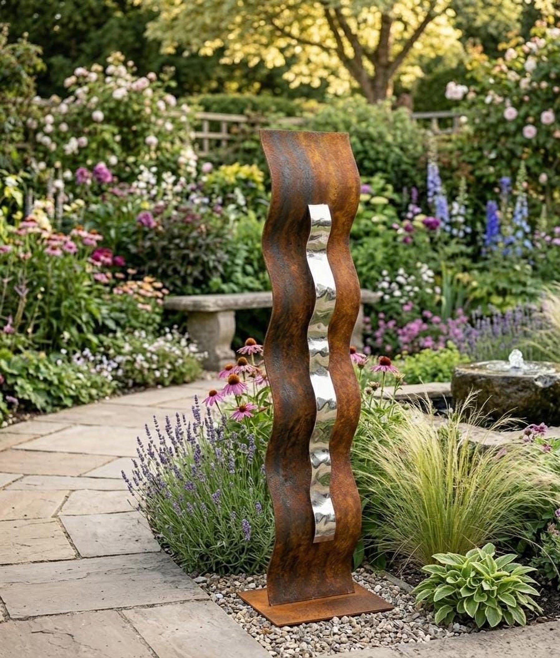 A rust-colored metal sculpture with a curved, wavy design stands in a lush garden filled with colorful flowers and greenery.