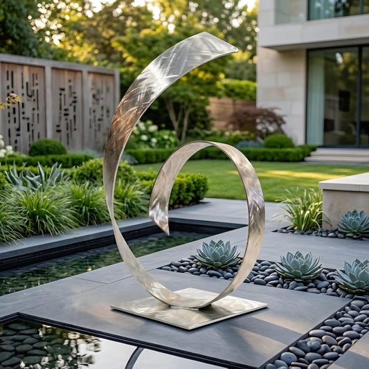 a modern garden sculpture with a unique, curving design that resembles a spiral or a wave. The sculpture is situated in a garden setting with a pond, surrounded by lush greenery and rocks.