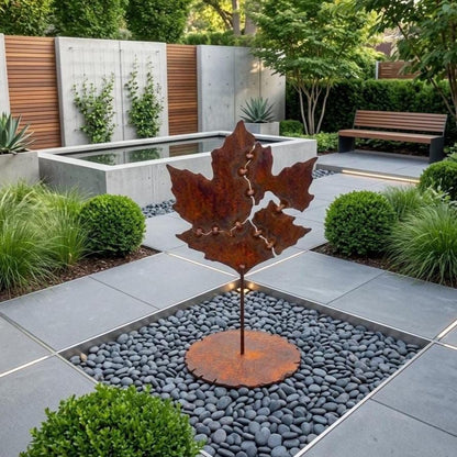 a modern garden design with a large metal sculpture of a leaf-shaped object placed in a gravel area surrounded by plants and shrubs.
