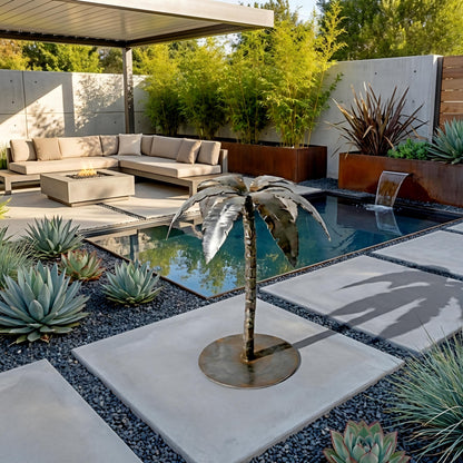 A modern outdoor living space with a seating area, a small pool, and a decorative metal sculpture of a palm tree. The space is surrounded by lush greenery and a stone pathway.