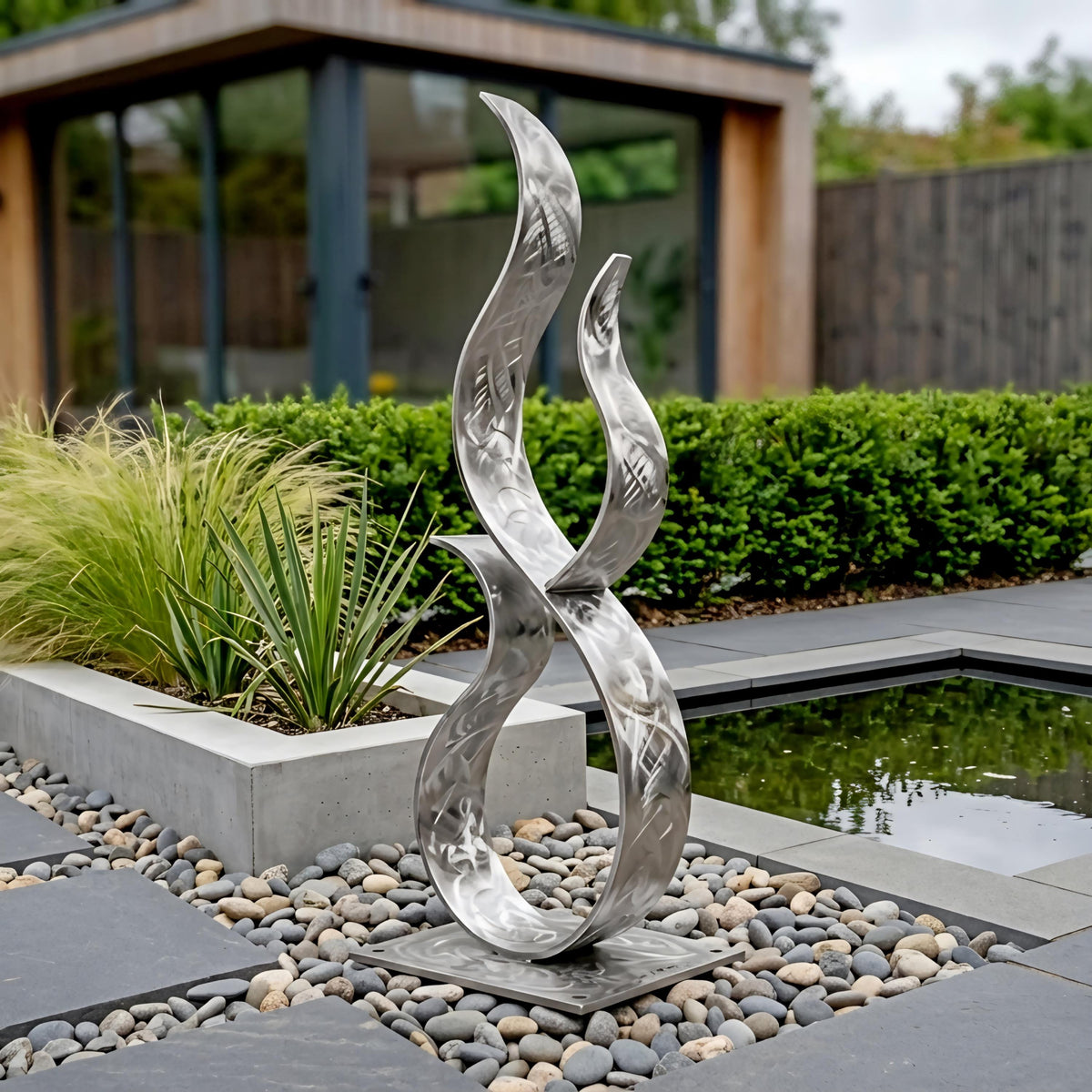 a modern metal sculpture with a unique, abstract design, situated in a garden setting with a pond and greenery in the background.