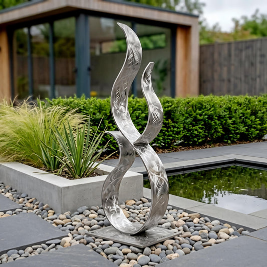 a modern metal sculpture with a unique, abstract design, situated in a garden setting with a pond and greenery in the background.