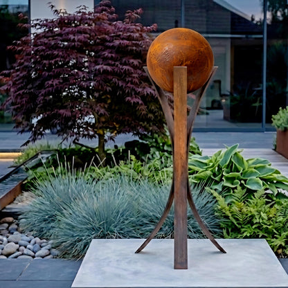 a garden with a large, round, orange sculpture of a ball on a stand, surrounded by various plants and shrubs.