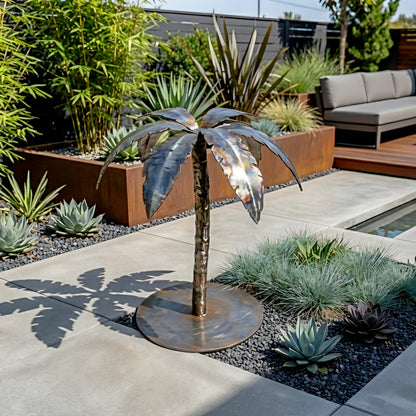a decorative metal sculpture of a palm tree, situated in a garden setting with various plants and a seating area.