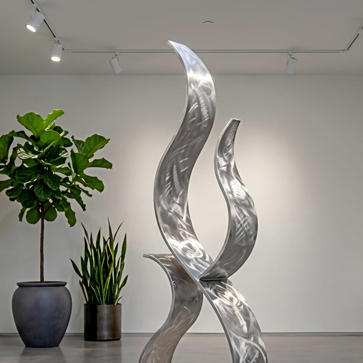 a modern art sculpture with a unique, abstract design, placed in a room with a white wall and track lighting. There are two potted plants in the room, one on the left side and the other on the right side, adding a touch of greenery to the space.