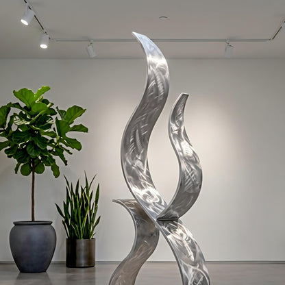 a modern art sculpture with a unique, abstract design, placed in a room with a white wall and track lighting. There are two potted plants in the room, one on the left side and the other on the right side, adding a touch of greenery to the space.