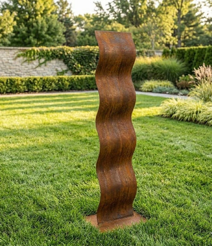a tall, rust-colored metal sculpture standing in a well-maintained, lush green lawn.