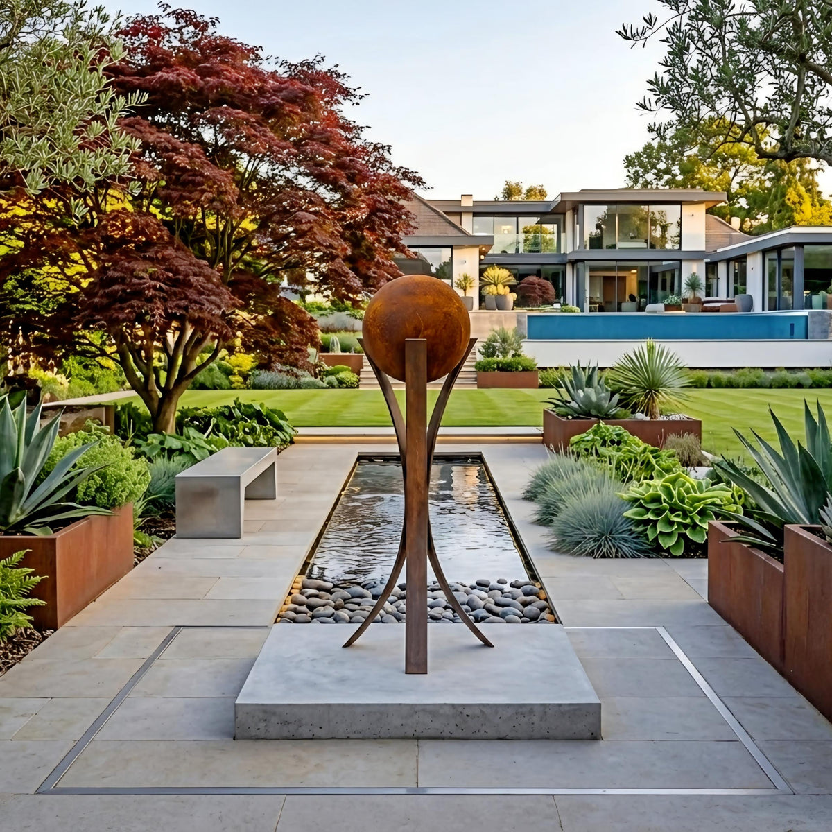 A modern garden with a large fountain, surrounded by lush greenery and a large tree. The garden is situated in front of a large house, creating a serene and inviting atmosphere.