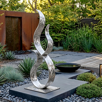 a modern garden sculpture with a unique, abstract design, situated in a well-maintained garden with a variety of plants and a small pond.