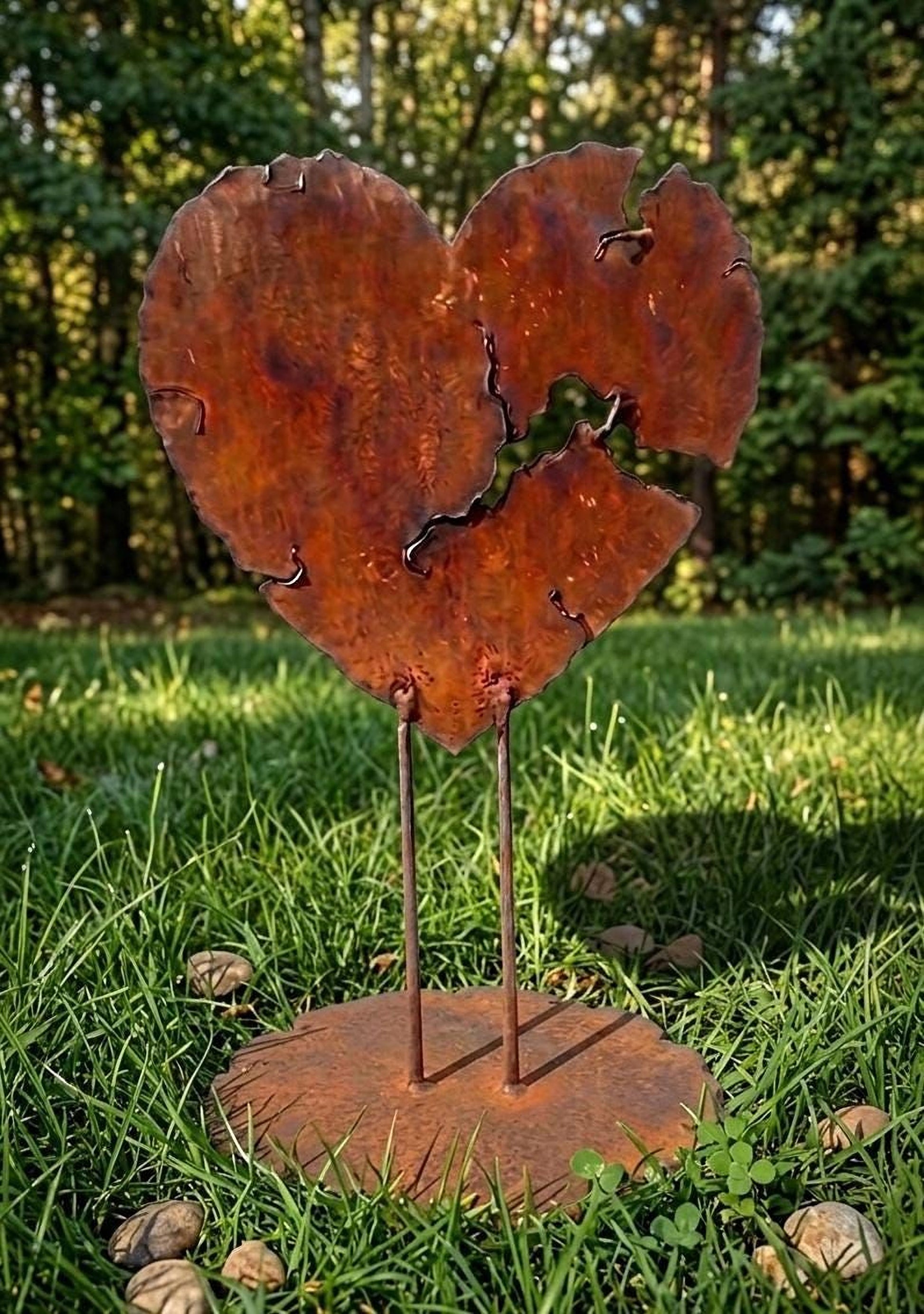 A rusted metal heart sculpture stands in a grassy area, surrounded by small rocks.