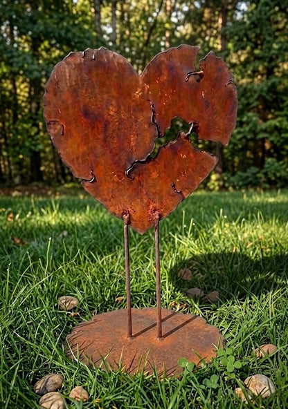 A rusted metal heart sculpture stands in a grassy area, surrounded by small rocks.